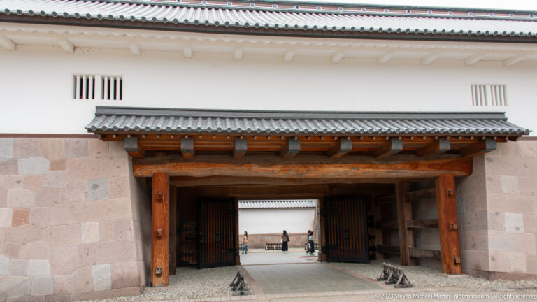 Large wooden gate beneath white castle walls with a view through to an inner courtyard.