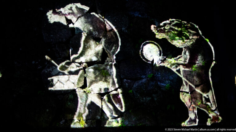 Two large projected figures face each other, one holding a round drum-like object.