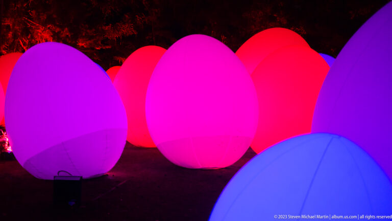 Overlapping magenta, red, violet, and blue glowing responsive ovoid forms at night.
