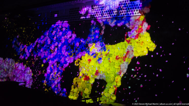 Blue-violet and yellow flower-formed animal projections composed of flower shapes on a stone wall.