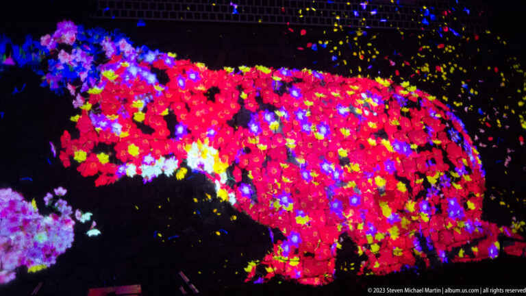 Large red quadruped-shaped projection composed of multicolored blossoms on stonework.