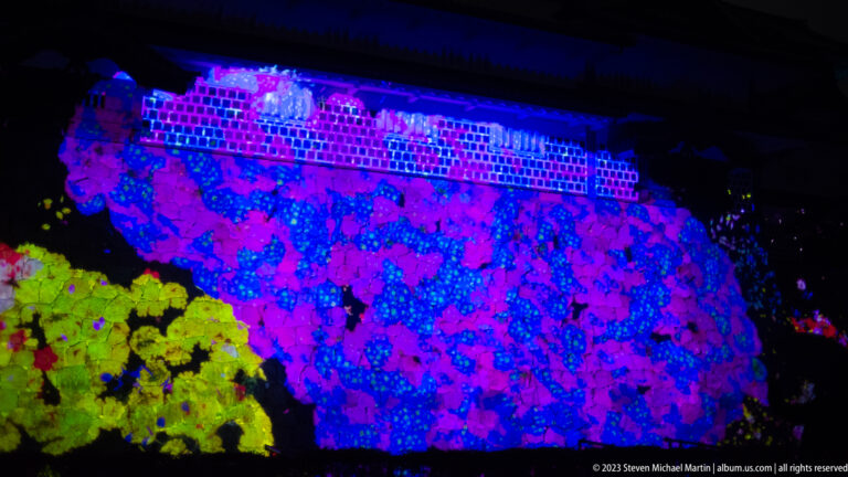 Large blue-violet flower-formed animal teamLab flower-animal projection beneath white castle walls.