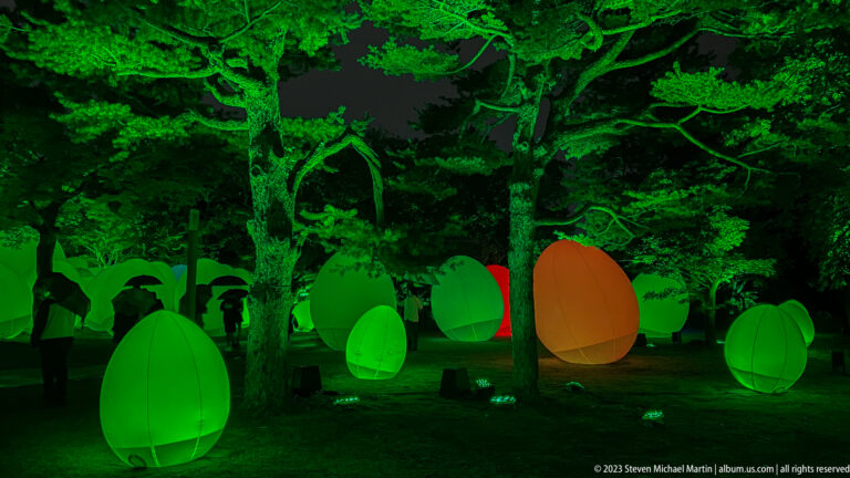 Green responsive glowing ovoids beneath illuminated trees, with one orange form among them.