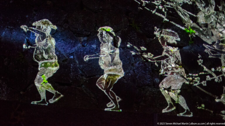 Three outlined human figures projected across dark, irregular castle stonework.