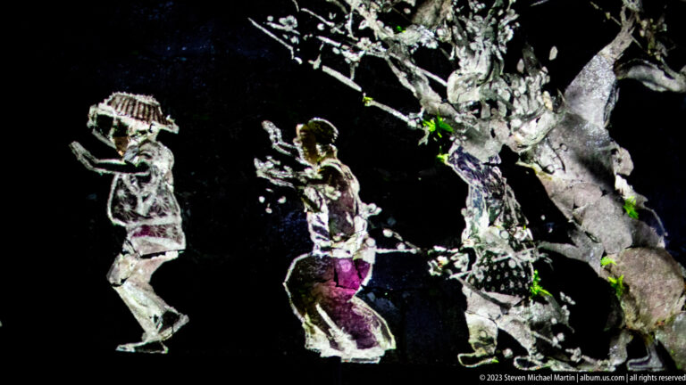 Two stylized figures and a branching tree projected on a dark stone wall.