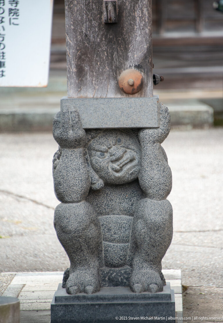Close view of a crouching carved stone figure supporting the base of a monument.