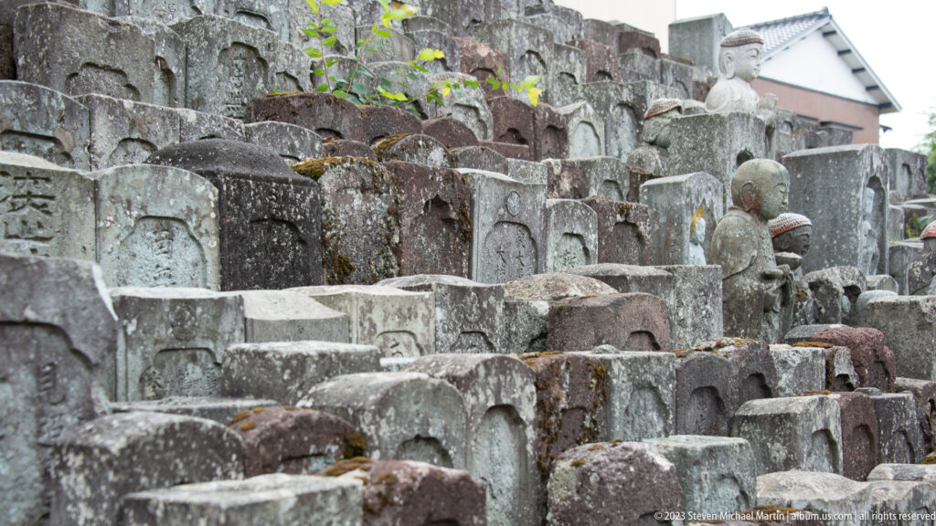 Dense rows of weathered stone grave markers and small Buddhist figures in a temple cemetery.