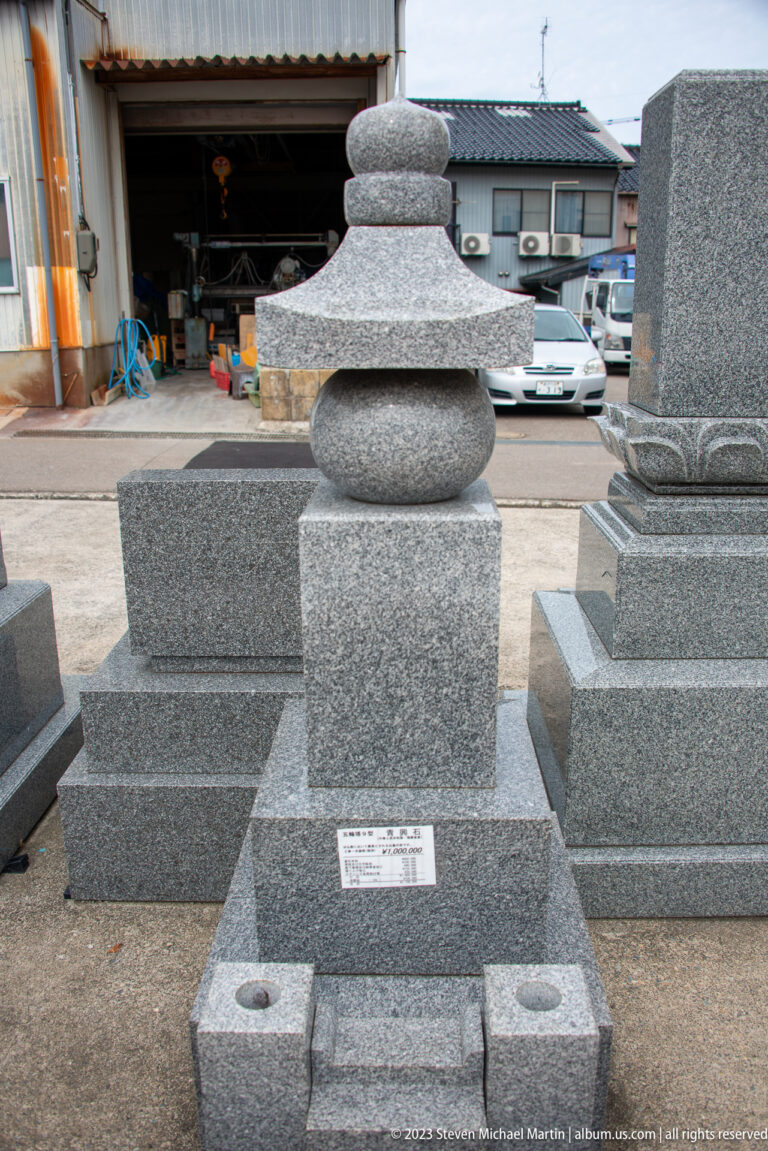 Polished gray granite grave monument displayed among other memorial stones in a workshop yard.