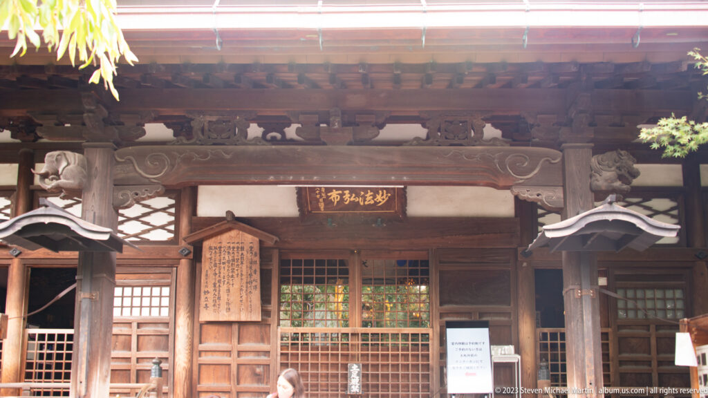 Wooden Buddhist worship hall façade with latticed doors, carved brackets, plaque, and posted notices.