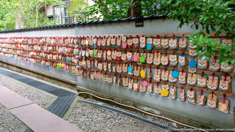 Long wall covered with rows of colorful animal-shaped wooden ema tied with red cords.