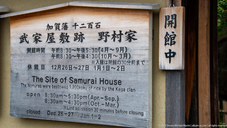 Bilingual visitor sign for the Nomura Samurai House with opening hours, closure dates, and adjacent open plaque.