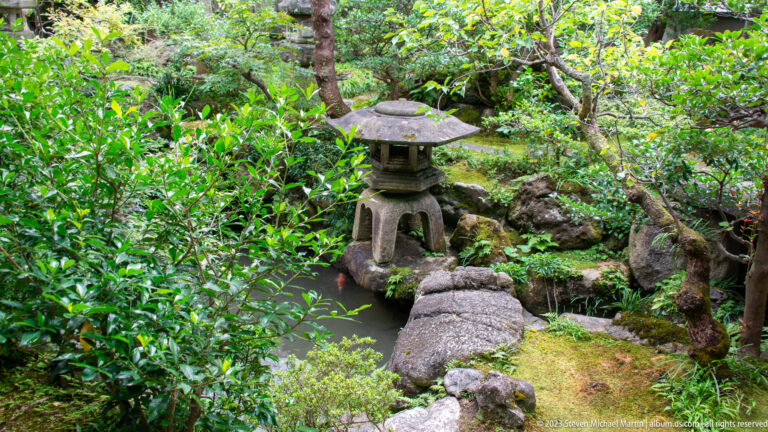 Squat stone lantern beside a narrow stepping-stone path in a lush mossy garden.