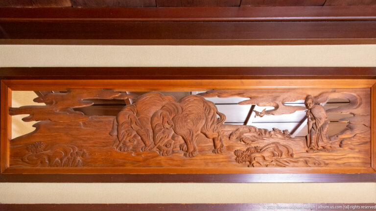 Carved wooden transom with a lion-like guardian, swirling forms, and a small human figure.