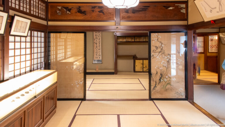 Connected tatami rooms with open sliding panels, painted fusuma, calligraphy, staggered shelves, shoji, and timber framing.