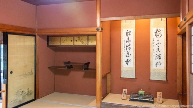 Tokonoma alcove with two calligraphy scrolls, built-in shelves, dark timber framing, and tatami floor.