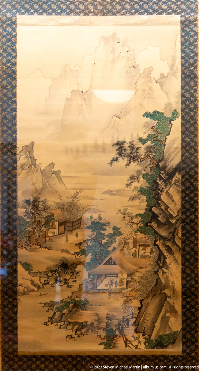 Japanese landscape painting with misty mountains, dark pines, water, and small buildings in the valley.