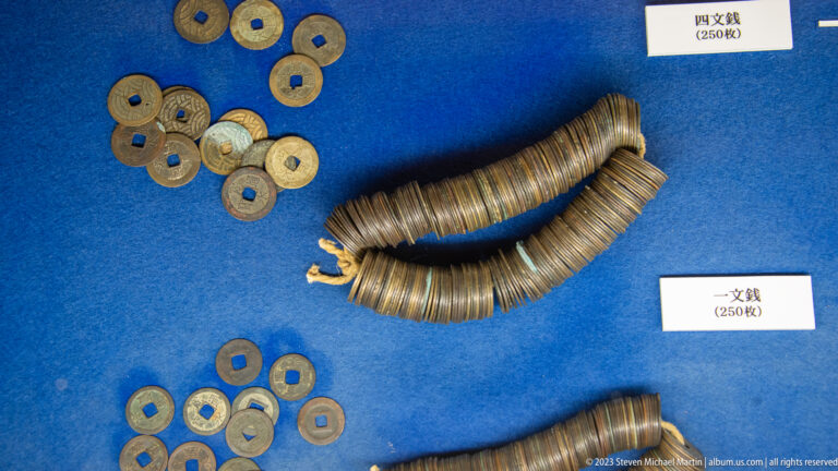 Groups of square-holed copper-alloy coins and two long bundled coin strings displayed on blue fabric.