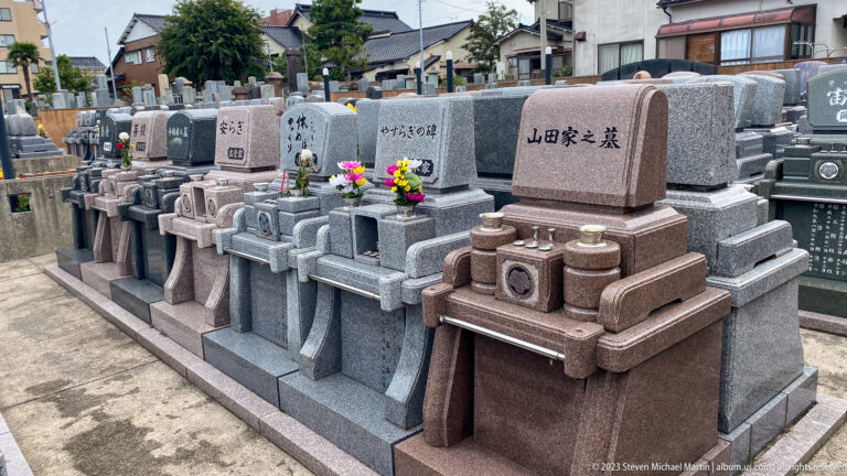 Rows of polished granite family graves with engraved names, offering tables, incense holders, and fresh flowers.
