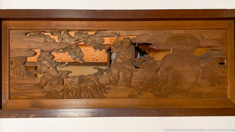 Carved wooden panel showing armored warriors among clouds, rocks, and pine branches.