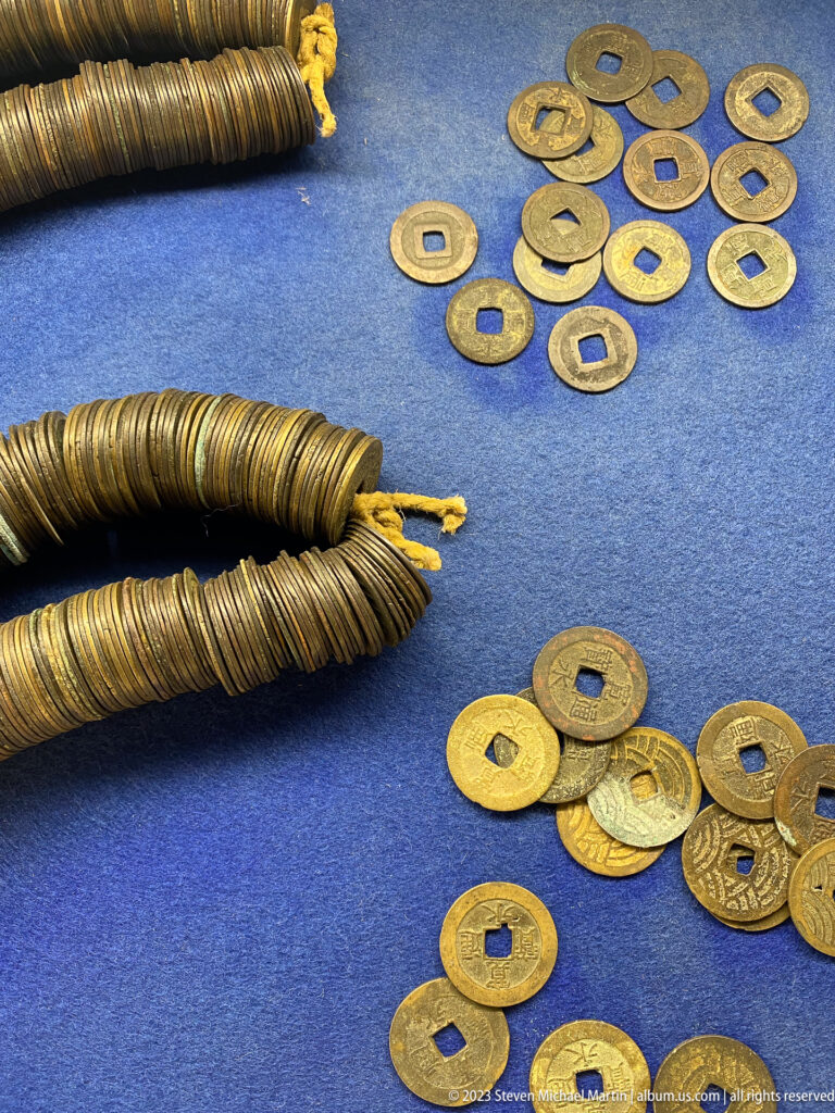 Round square-holed Japanese coins and two long bundled coin strings displayed on blue fabric.