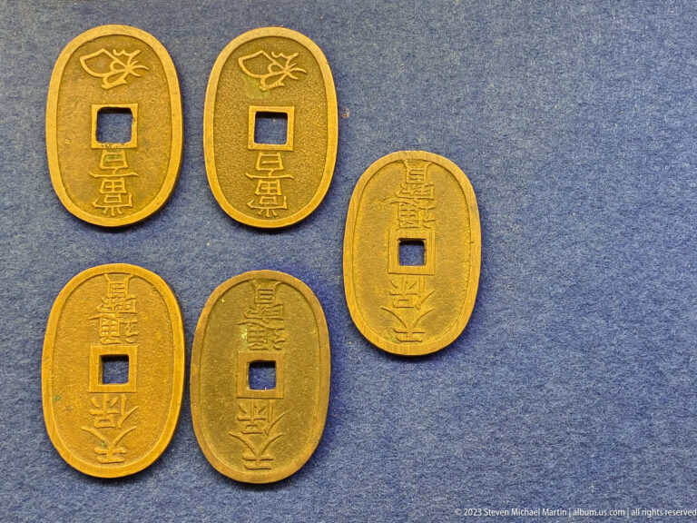 Five oval gold-toned Japanese coins with square central holes and vertical inscriptions.