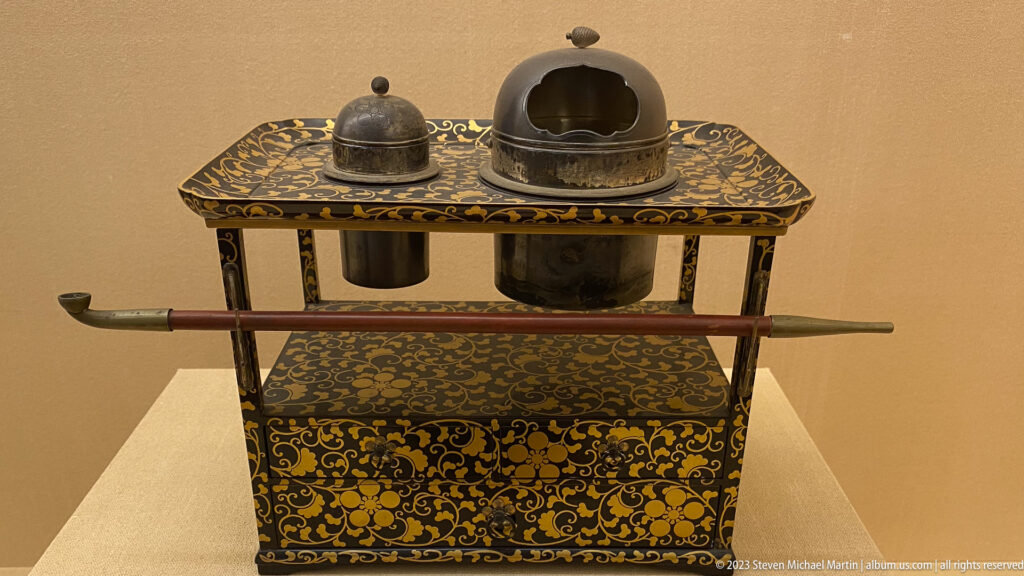 Black-and-gold lacquered stand holding two metal containers and a long sheathed implement.