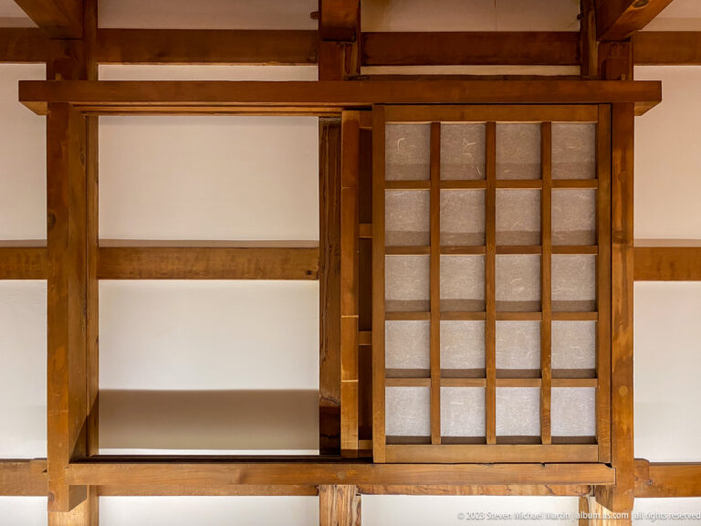 Exposed timber framing around white plaster wall and a small sliding lattice panel.