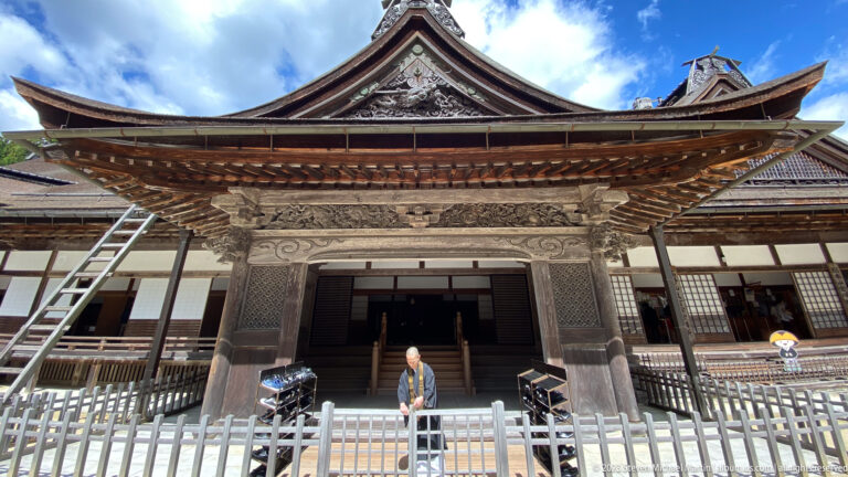 Ornate gabled entrance of Kongōbu-ji with carved timber details, steps, and a visitor.