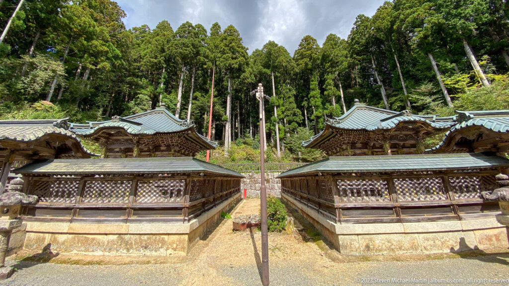Paired Tokugawa mausoleums on stone bases beneath tall cedars at Koyasan.