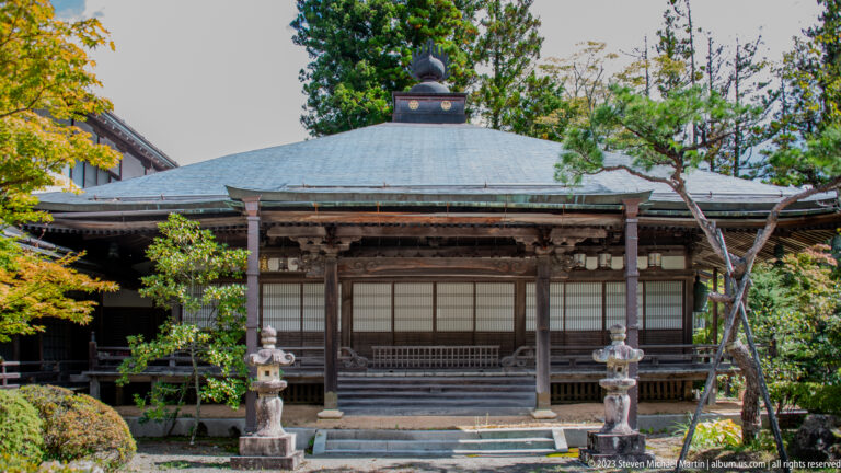 Wooden temple hall with hipped roof, veranda, sliding screens, stone lanterns, and landscaped garden.