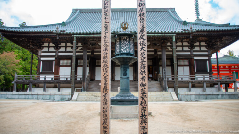 Bronze lantern centered before Kondo Hall between two tall inscribed wooden pillars.