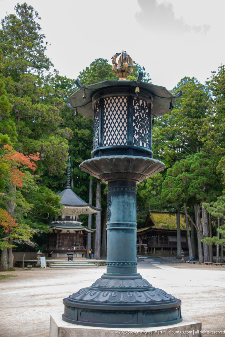 Large bronze temple lantern with lattice chamber and broad cap standing in an open courtyard.