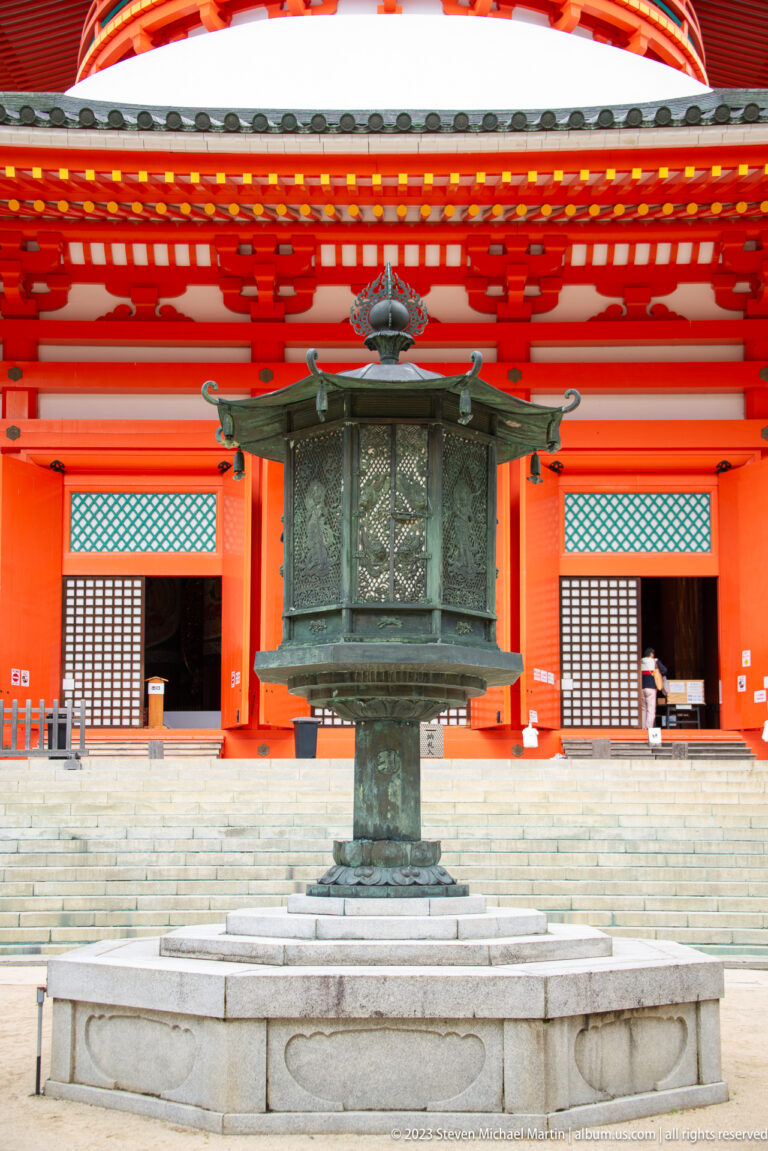 Large bronze incense burner centered on stone steps before the vermilion Konpon Daitō.