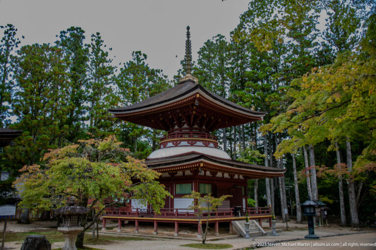 Two-story red-and-white timber pagoda with square roofs and finial among trees.