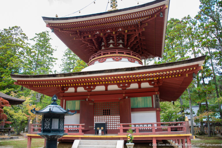 Close view of a red-and-white two-story pagoda with veranda, lattice doors, and black lantern.