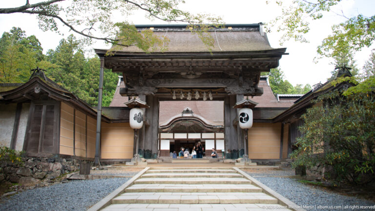 Frontal view of Kongōbu-ji’s timber main gate with white lanterns, ocher walls, and stone path.