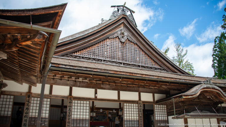 Broad Kongōbu-ji temple façade with bark roof, lattice gable, sliding screens, and open entrance.
