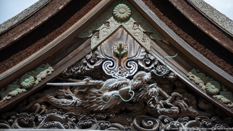 Ornate wooden dragon carving with clouds and waves filling a triangular temple gable.