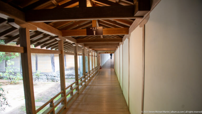 Long covered wooden corridor with exposed rafters, white walls, and open railing at Kongōbu-ji.
