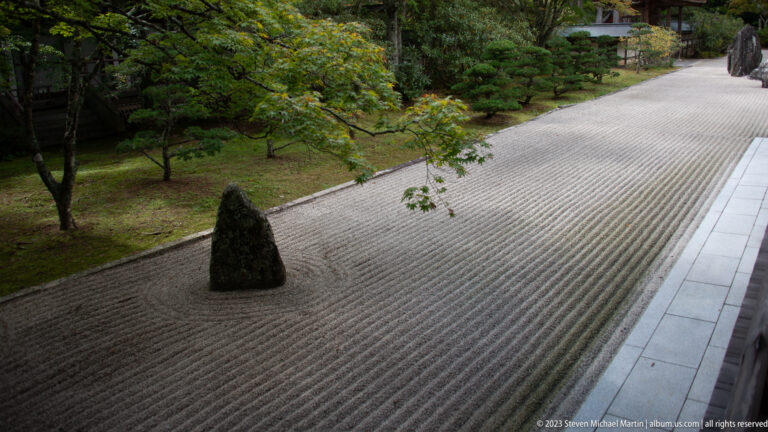 Raked white gravel garden with one upright dark stone viewed from a temple veranda.
