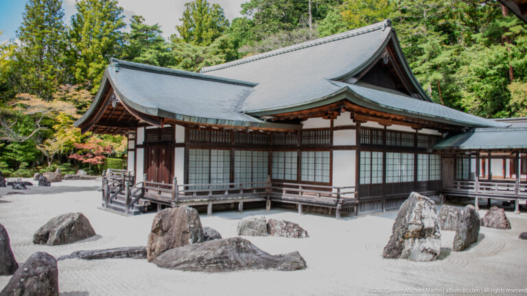 Raked rock garden with multiple stones beside a white-and-timber temple hall at Kongōbu-ji.