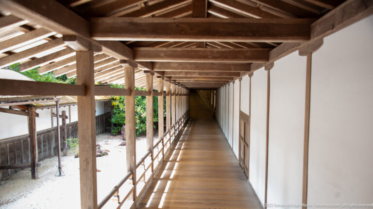 Long sunlit wooden corridor with exposed rafters, open railing, and white wall at Kongōbu-ji.