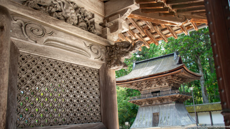 Carved wooden bracket and lattice screen in the foreground with a traditional temple gate beyond.