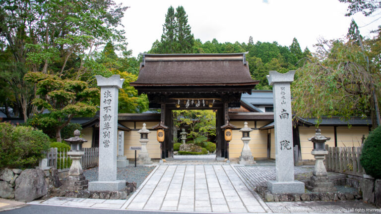 Nanin temple gate between inscribed stone pillars, with lanterns and a paved approach into the garden.