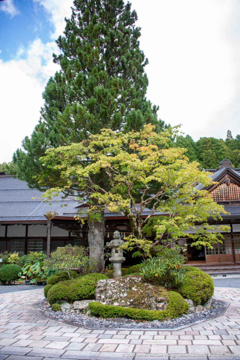 Landscaped Nanin courtyard with mature trees, clipped shrubs, stone lantern, and low temple buildings.