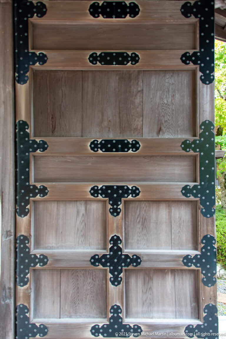 Close view of a pale timber door covered with black decorative iron straps and hinge plates.