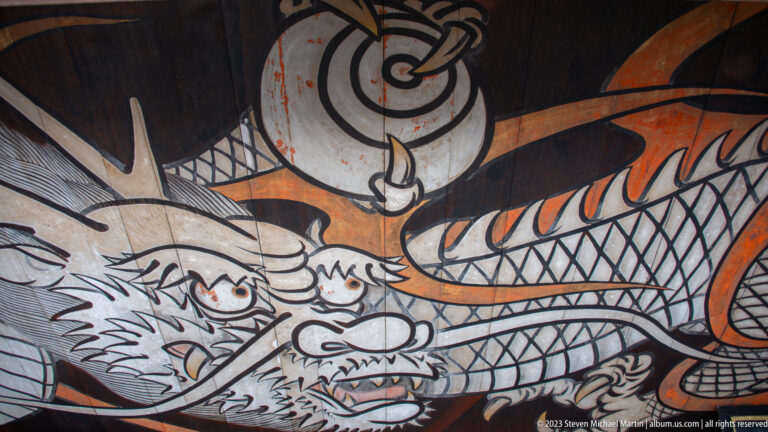 Close-up of a large painted dragon in black, white, and orange with claws and coiling scales.