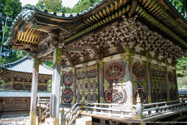Oblique view of an ornate timber shrine with carved doors, painted panels, and deep bracketed eaves.