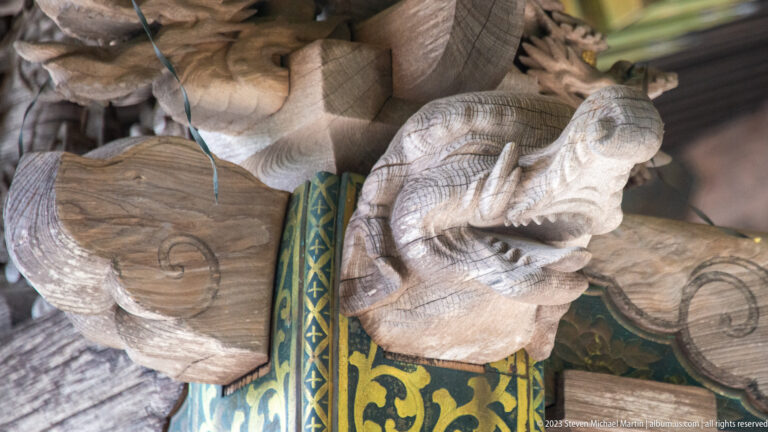 Close-up of a carved elephant-like bracket figure with curled trunk above green-and-gold ornament.