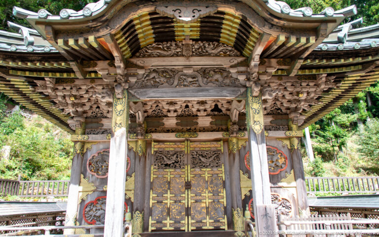 Frontal view of an ornate shrine with carved doors, gilded fittings, and dense bracket work.